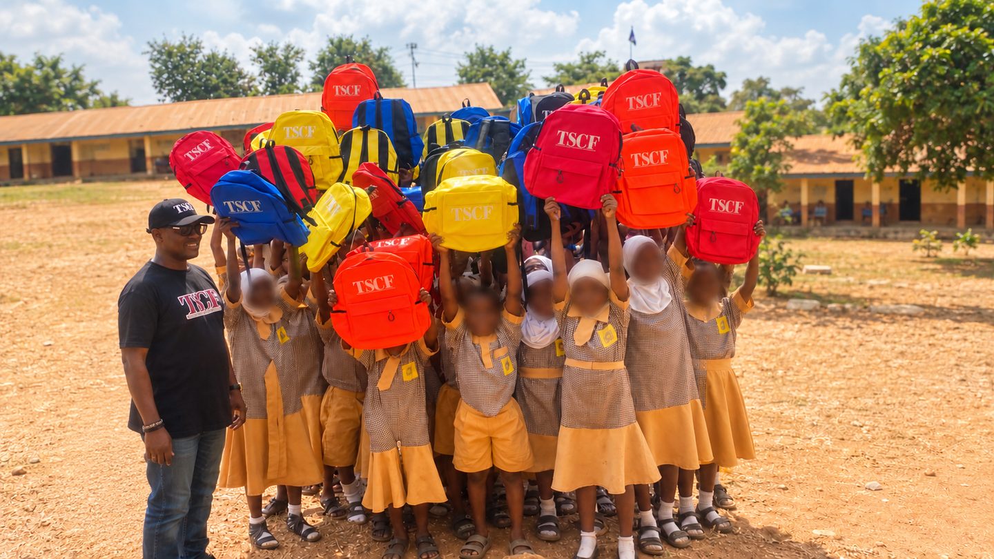 Children holding up colorful TSCF backpacks at a school supply drive in Nigeria